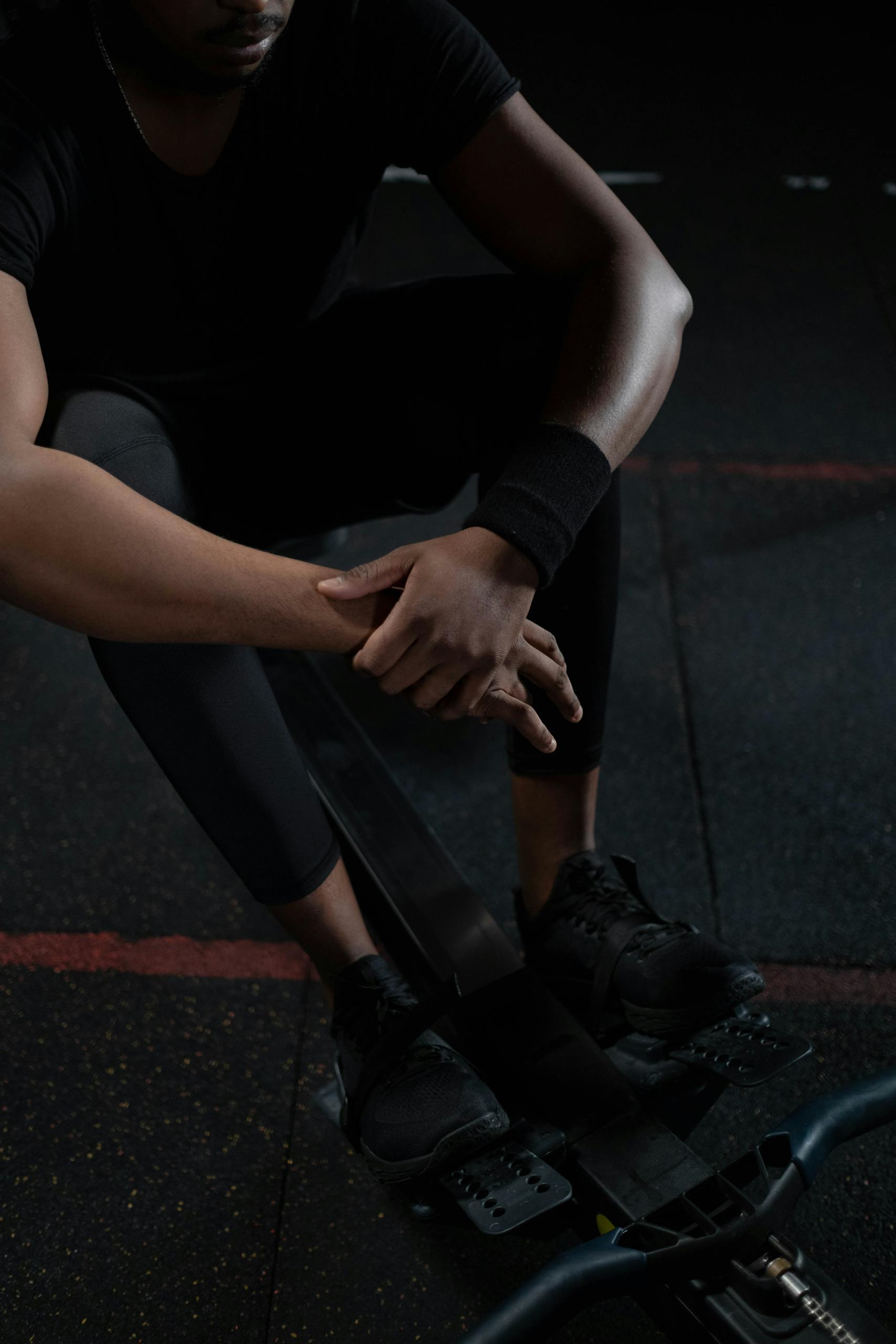 A man in sportswear resting on a rowing machine in a dimly lit gym setting.