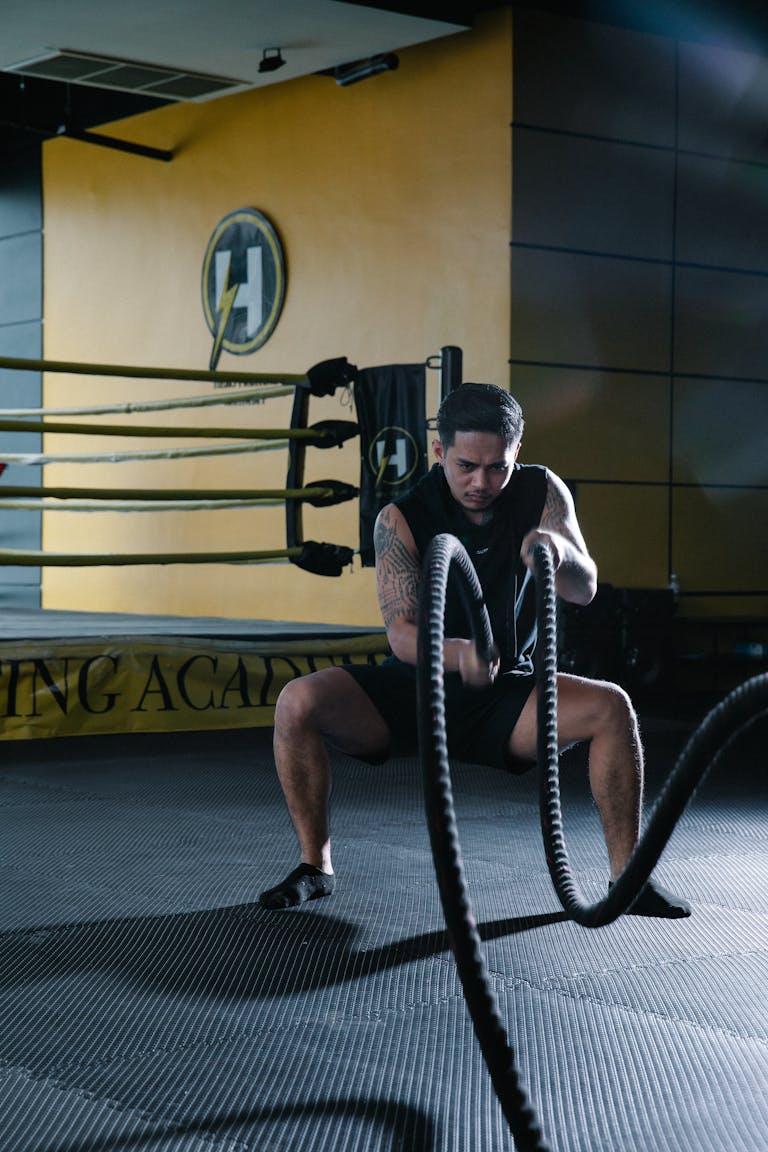 A man intensely performing battle rope exercises in a modern gym.