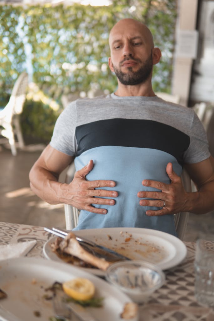 A man sits back feeling full after dining, showing a satisfied expression while touching his stomach.
