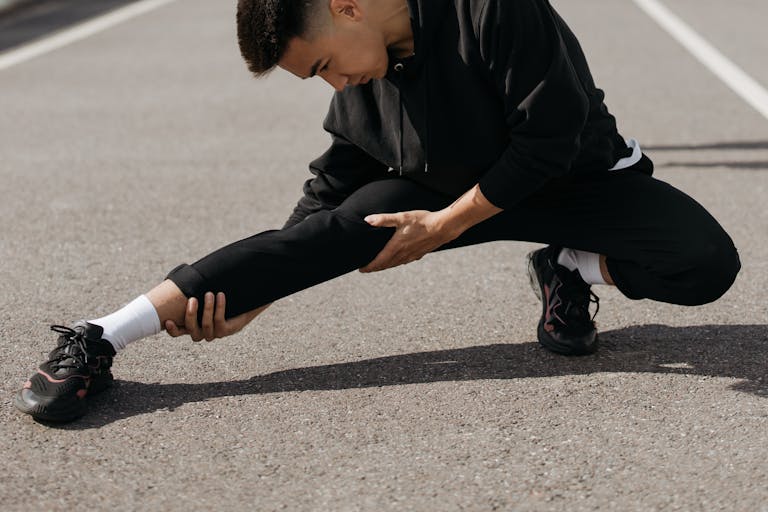 A young man performs stretching exercises on a city street, focusing on flexibility and fitness.