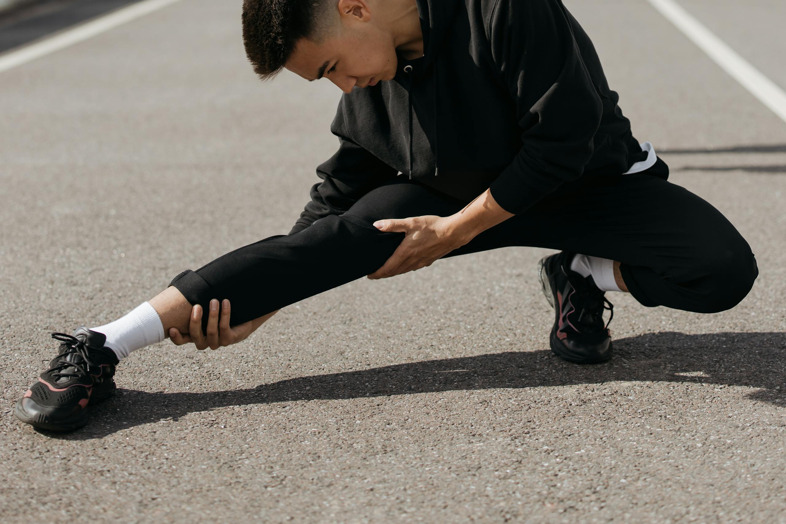 A young man performs stretching exercises on a city street, focusing on flexibility and fitness.