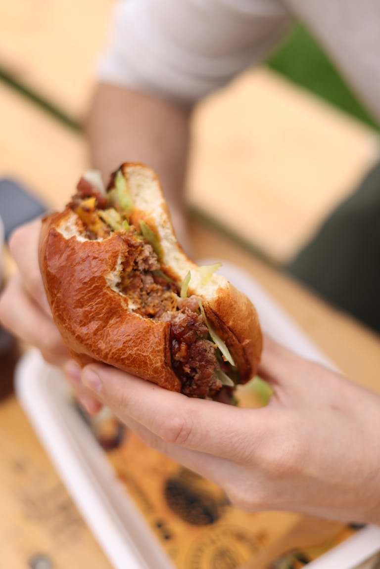 Appetizing beef burger with fresh ingredients being held by a diner outdoors.
