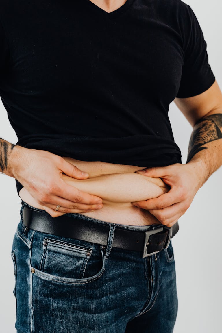 Close-up of a man in a black shirt displaying tattoos while pinching his belly skin.