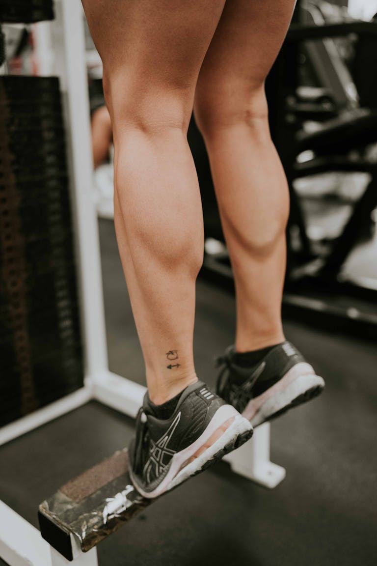 Close-up of a woman doing calf raises at the gym, focusing on muscular legs.