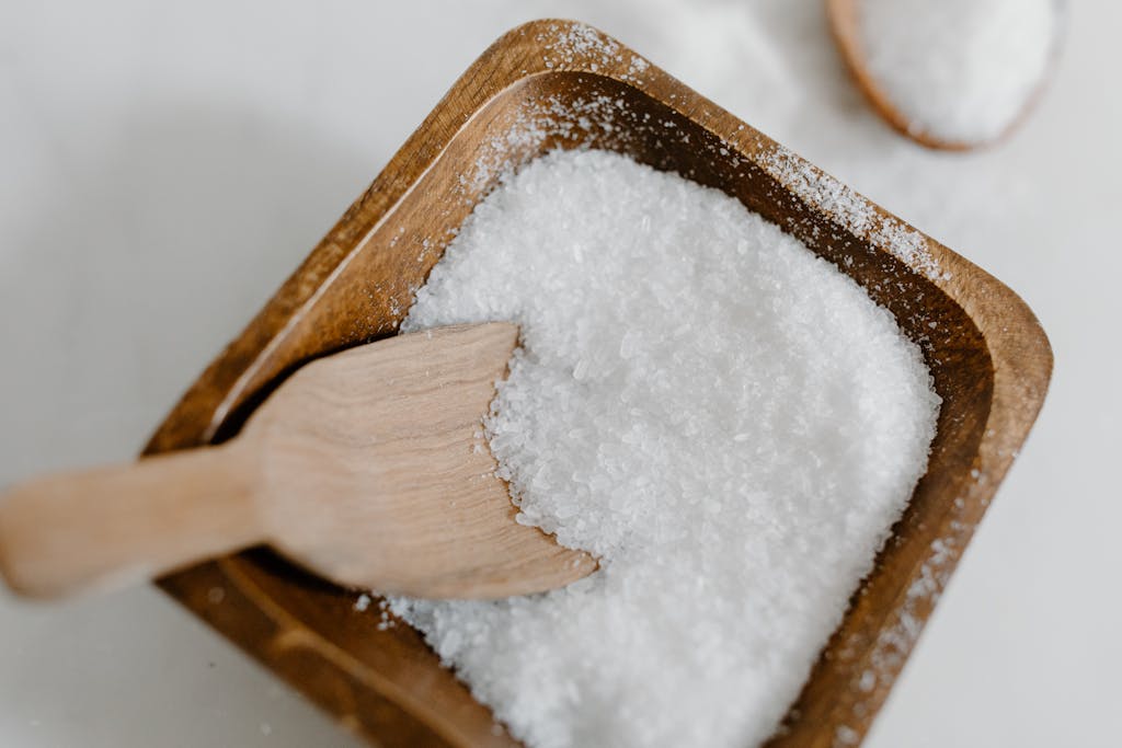 Close-up of coarse sea salt in a wooden bowl with a wooden scoop, perfect for culinary use.