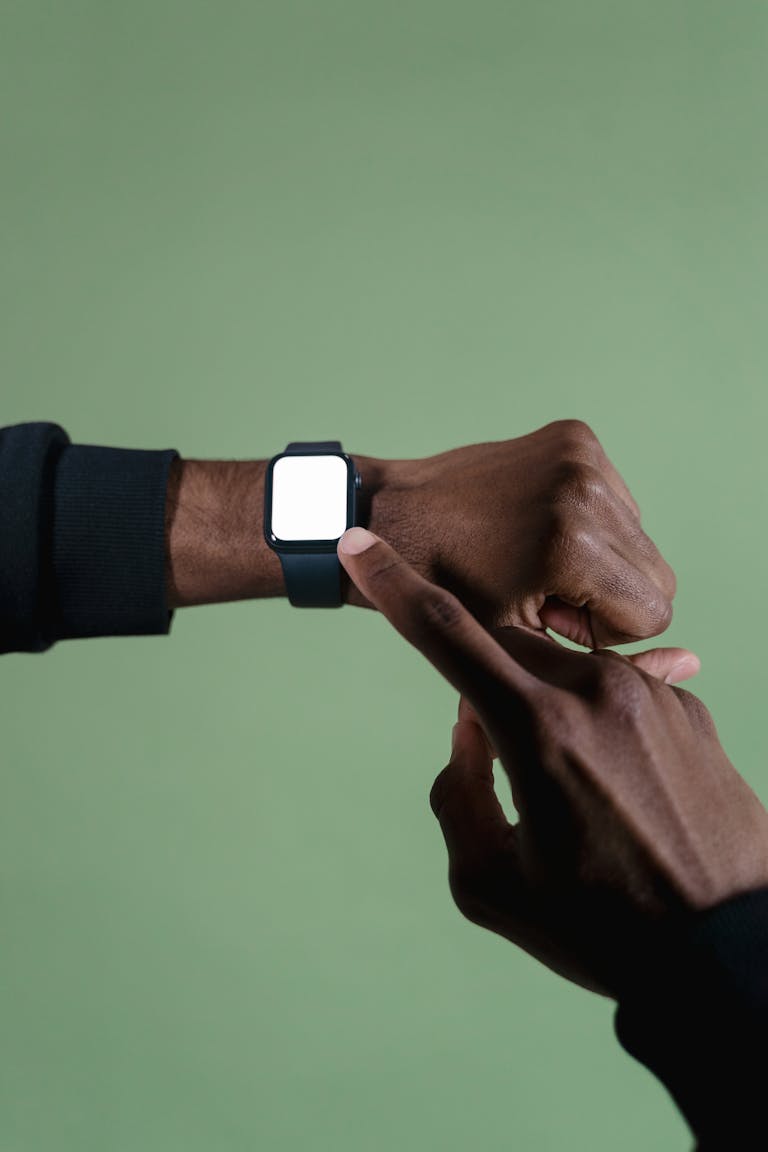 Close-up of hands pointing at a smartwatch on a wrist against a green background.