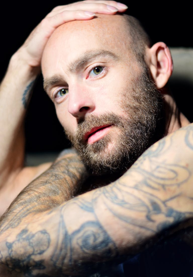 Close-up portrait of a bald man with a beard and tattoos, exuding confidence and introspection.