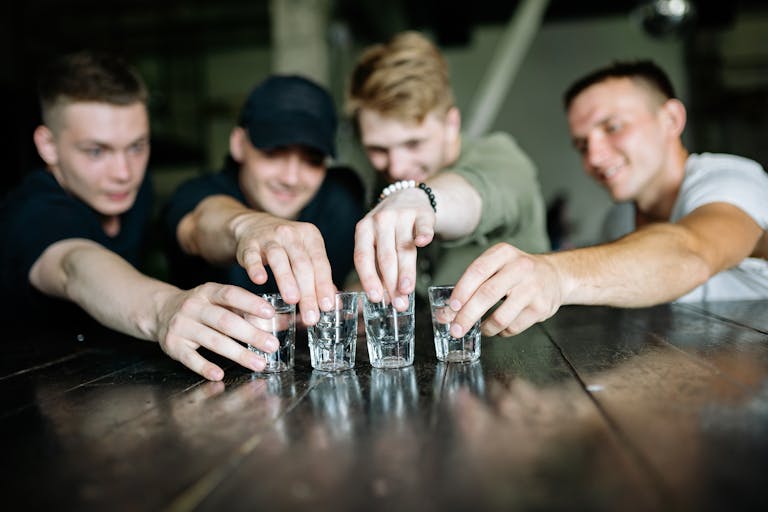 Group of friends reaching for shot glasses, having fun indoors.