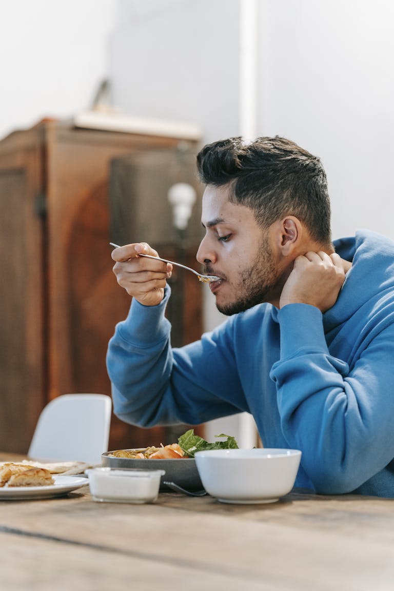 Man in a blue hoodie enjoying a fresh meal at home.