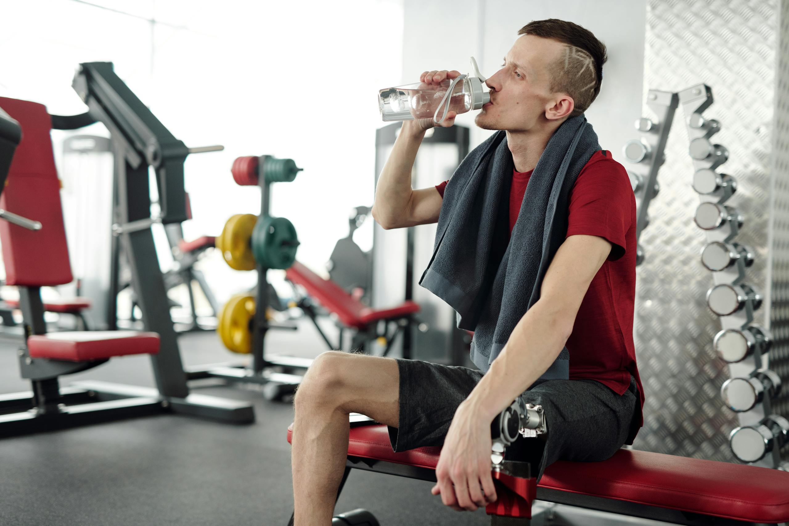 Man with prosthetic leg rests on bench and drinks water during gym workout.