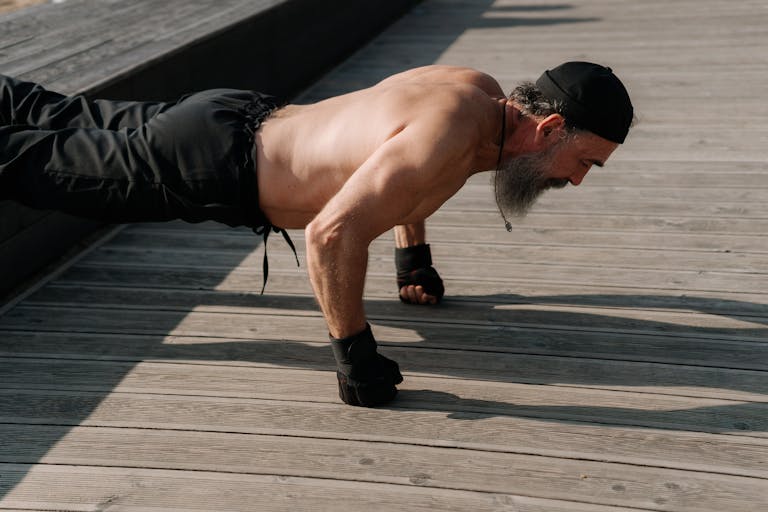 Senior man with a beard exercising outdoors, performing push-ups on a wooden deck.