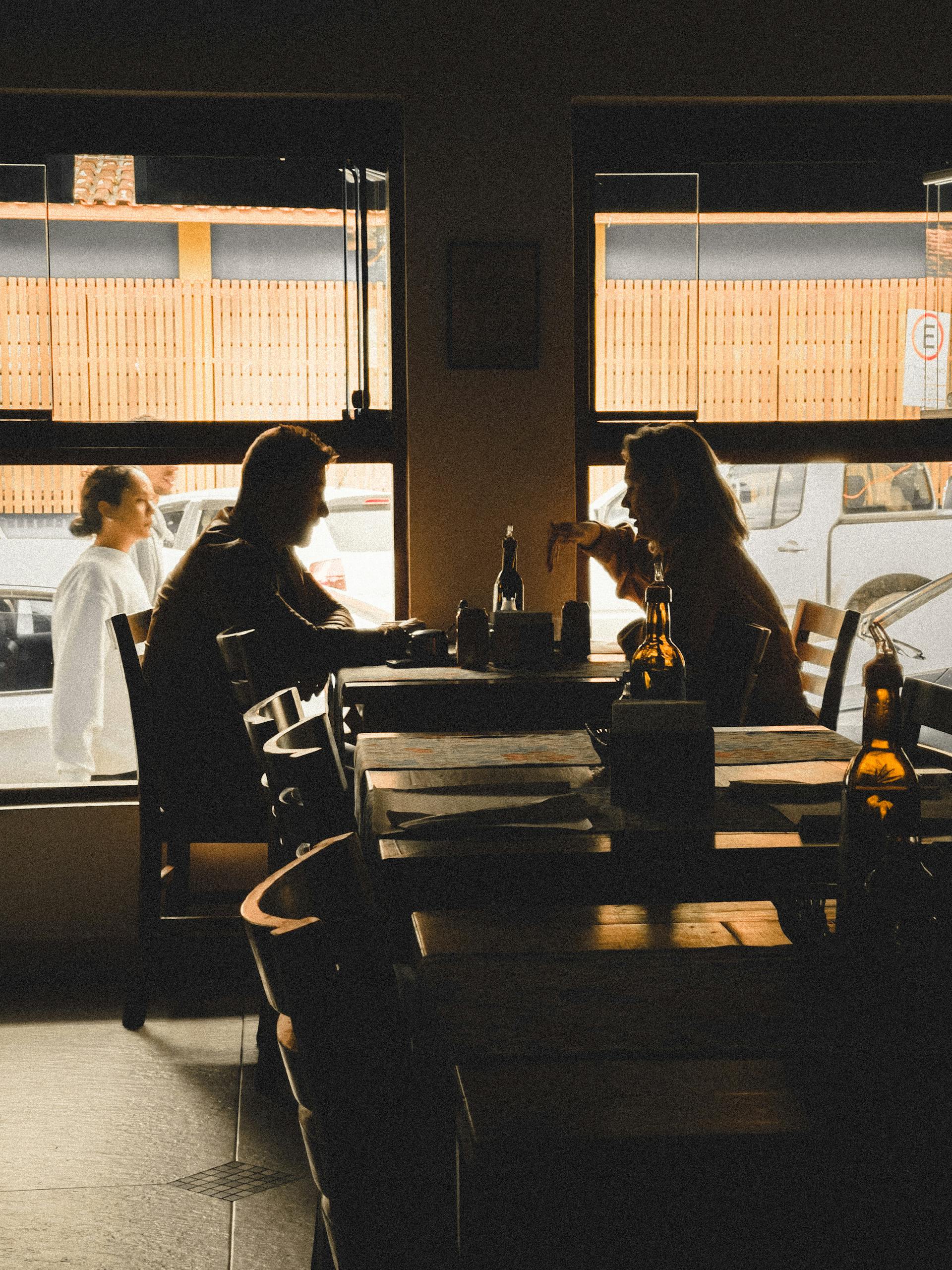 Silhouette of a couple sharing a moment at a cafe as the sunlight filters in through the window.