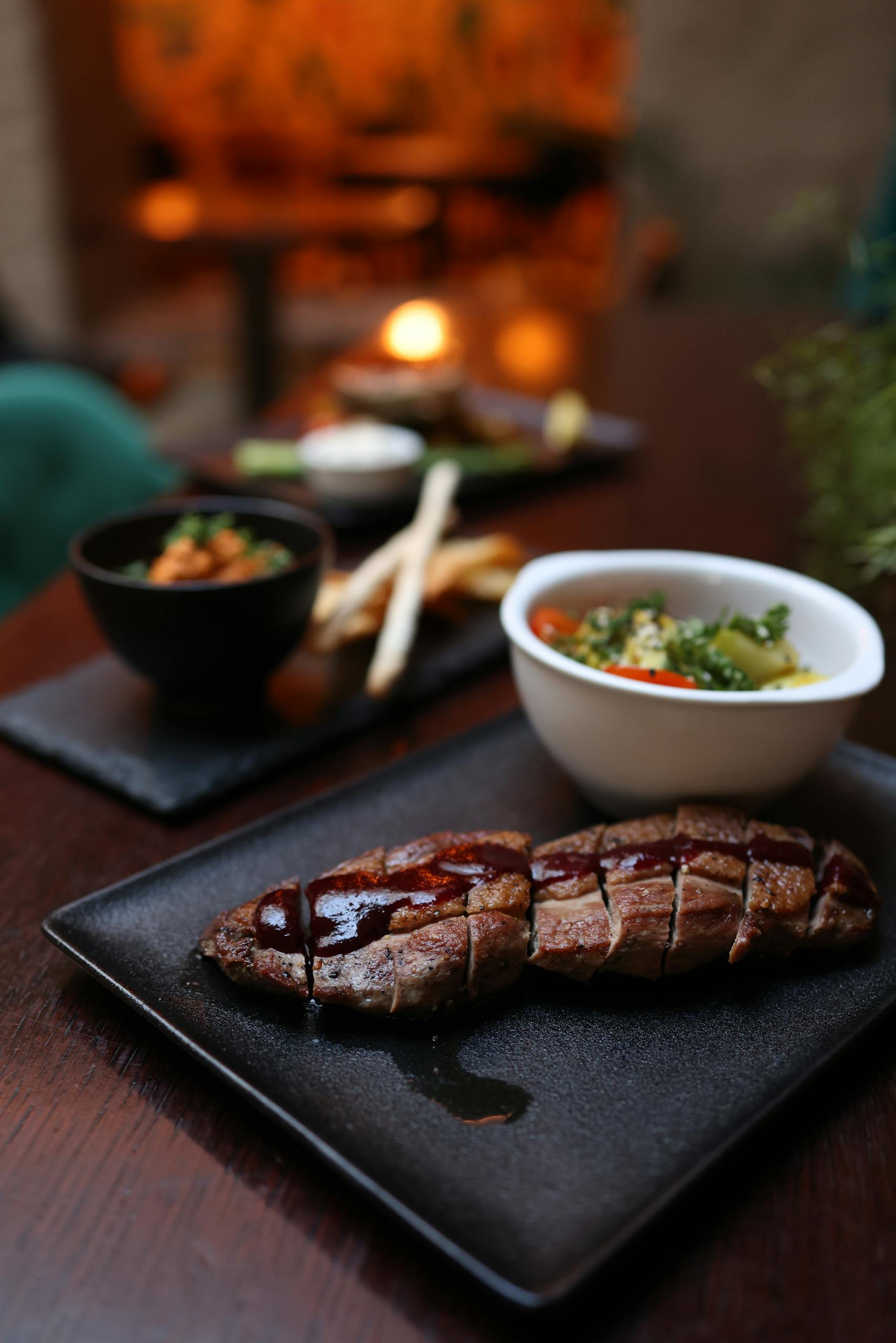 Sliced steak with sauce, side dishes in warm, intimate dining setting.