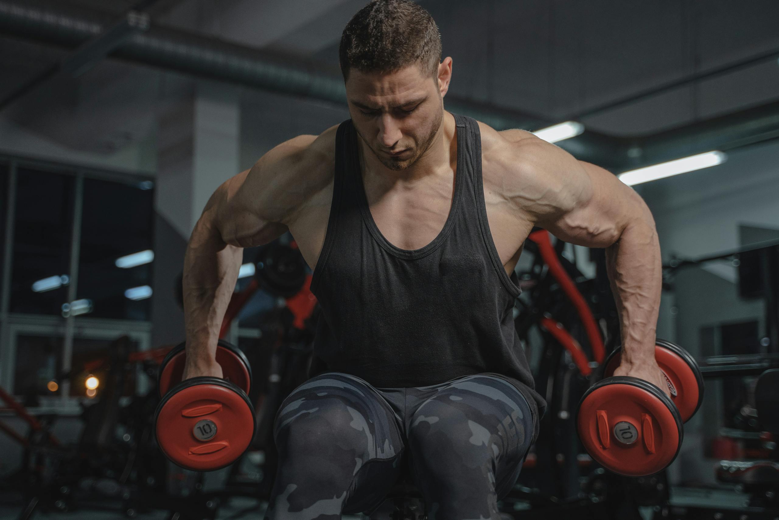 Strong man in gym lifting dumbbells, showcasing muscular physique and fitness dedication.